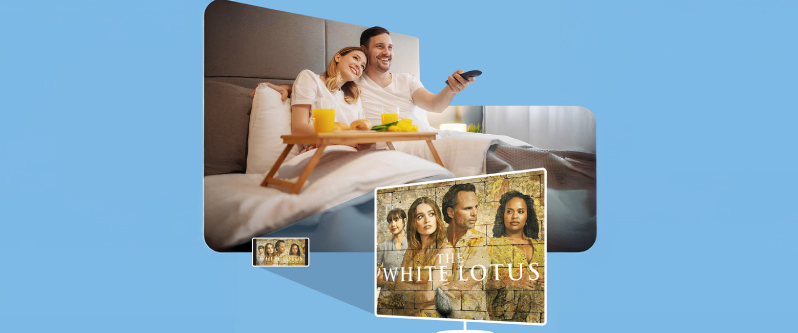 Couple enjoying streaming content, watching "The White Lotus" on IPTV in a hotel room, with breakfast in bed and a cozy atmosphere.