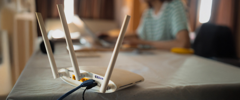 A wireless Wi-Fi router with three antennas on a table, person working in the background